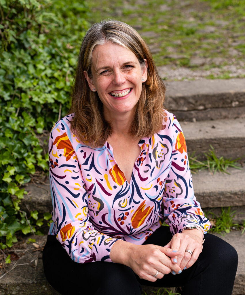 Photograph of Claire Bradshaw sitting on a step outdoors smiling