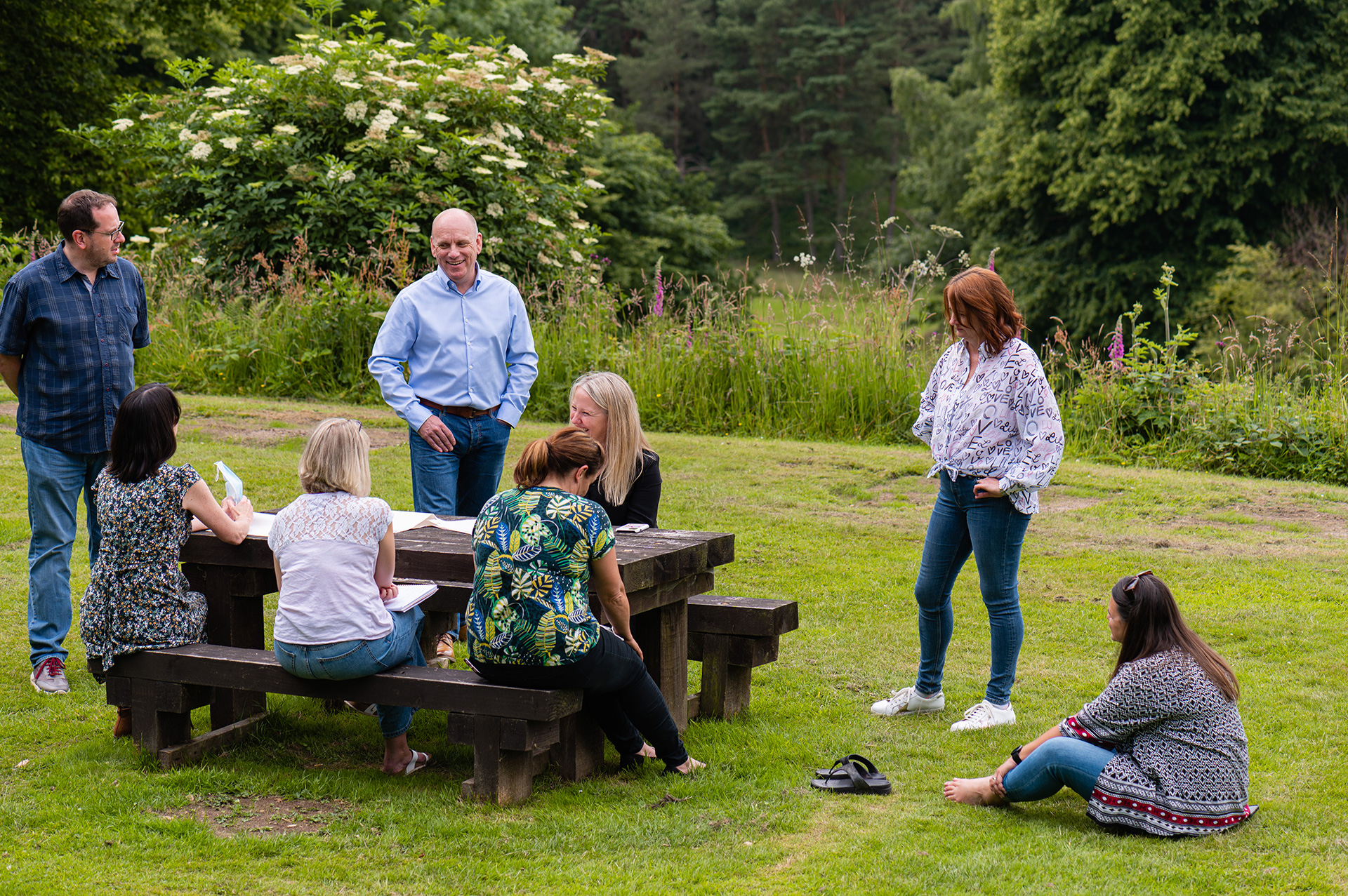 People in the gardens of Shrigley Hall having a discussion around a picnic bench in the summer surrounded by nature